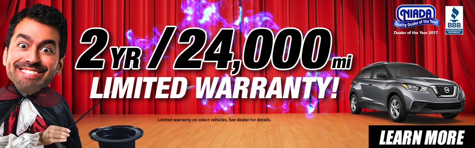 A man dressed as a magician stands next to text promoting a 2-year, 24,000-mile limited warranty, with a car and a 